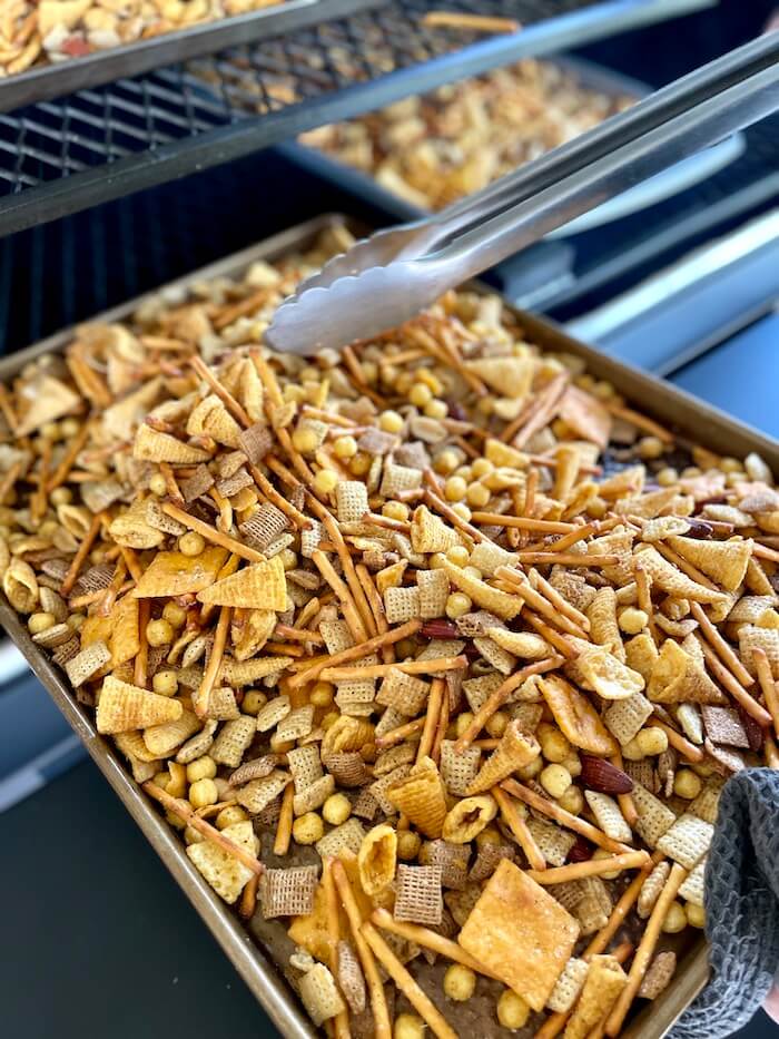 mixing smoked Chex mix on a sheet tray on a grill