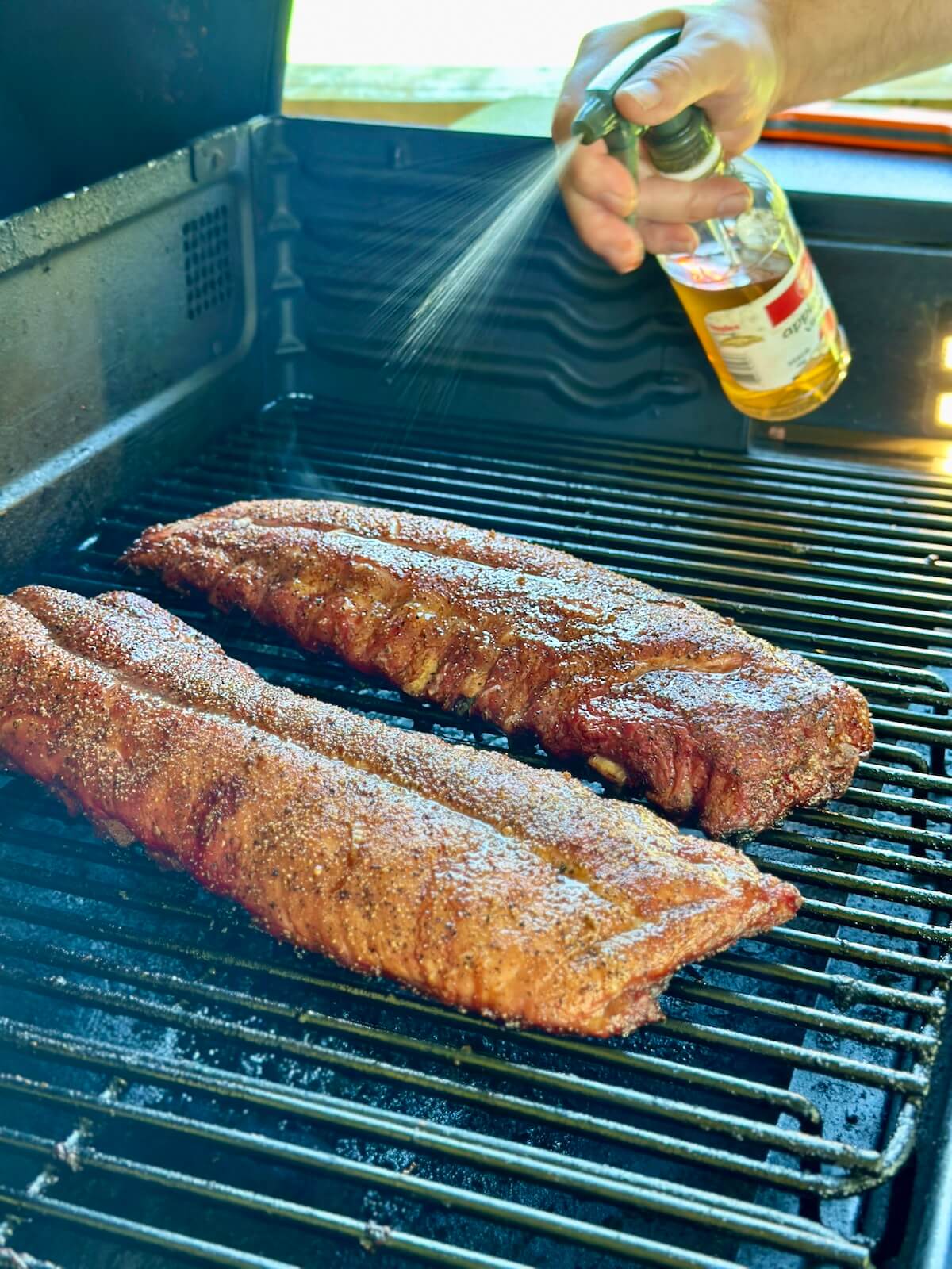 spritzing smoked pork ribs on a Traeger