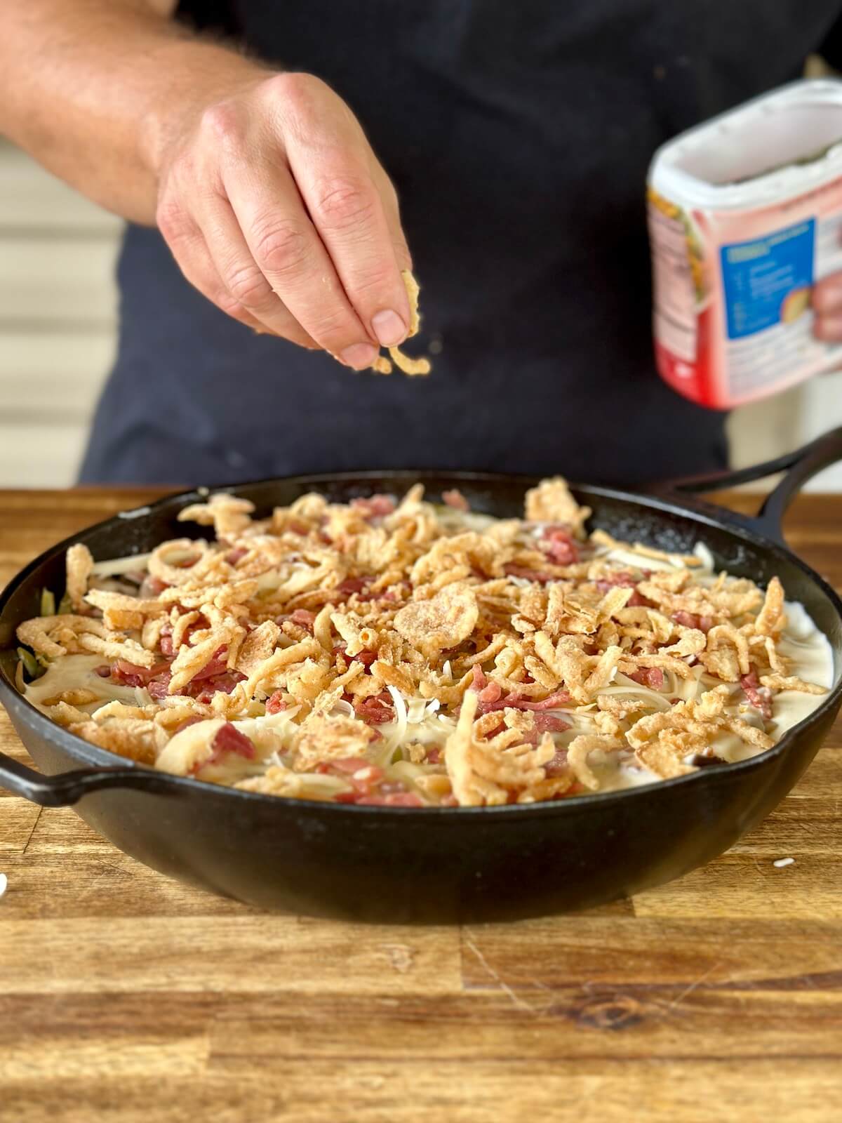 sprinkling a green bean casserole with crispy fried onions