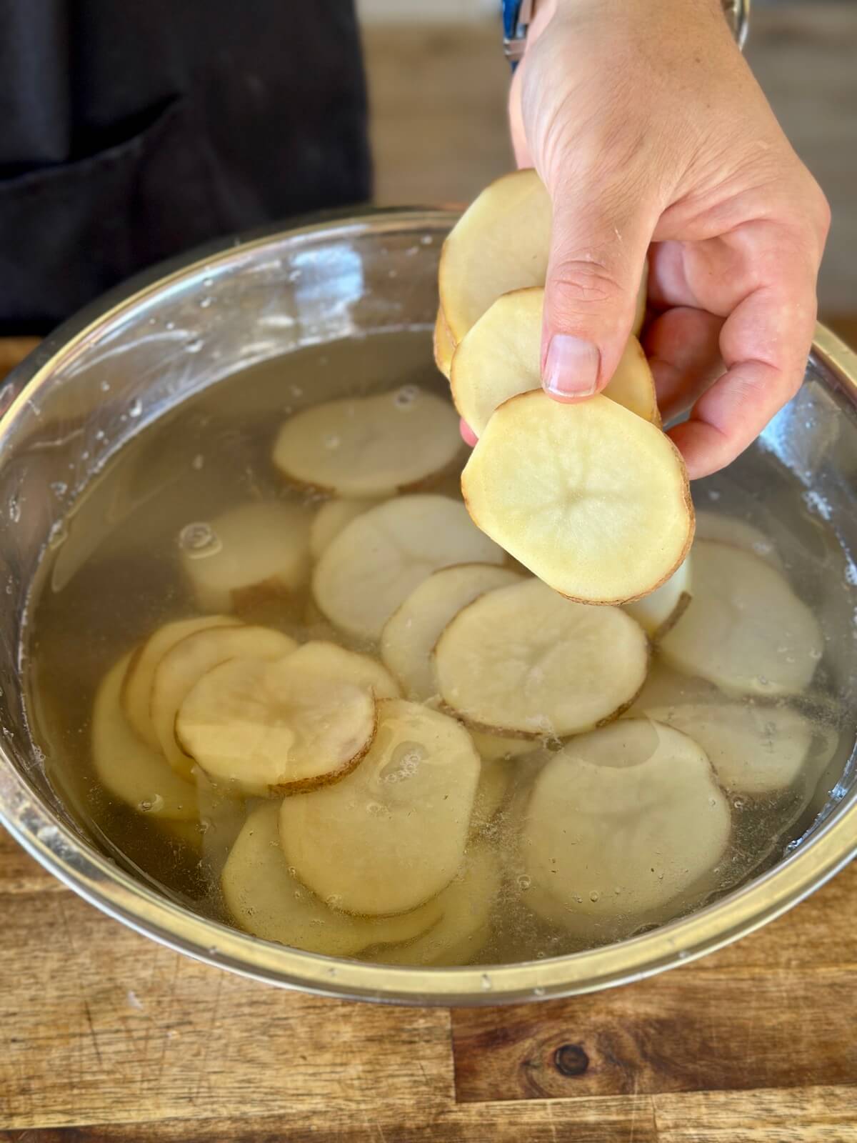 adding sliced potatoes to a bowl of water