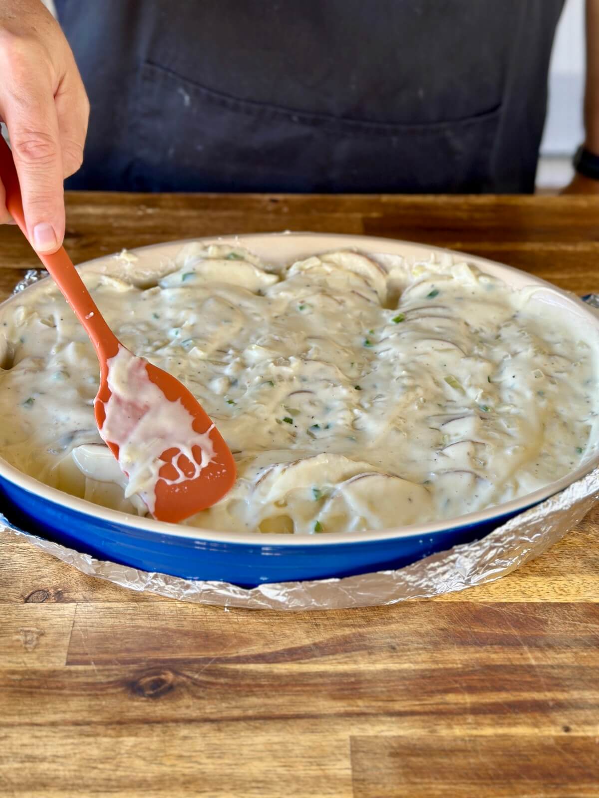 spreading cream sauce on top of sliced potatoes in a casserole dish