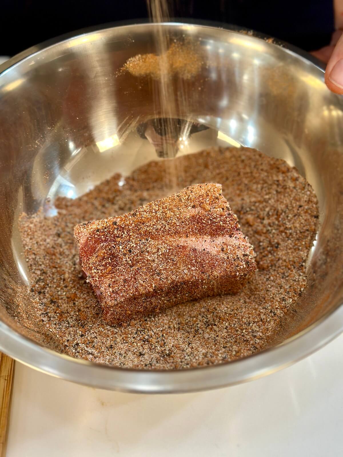 adding a curing mixture to pork butt pieces