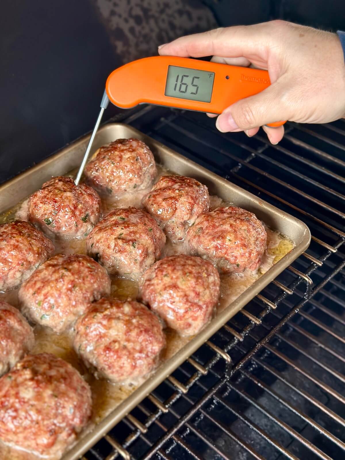 using an instant read thermometer to check the internal temperature of smoked meatballs on a pellet grill