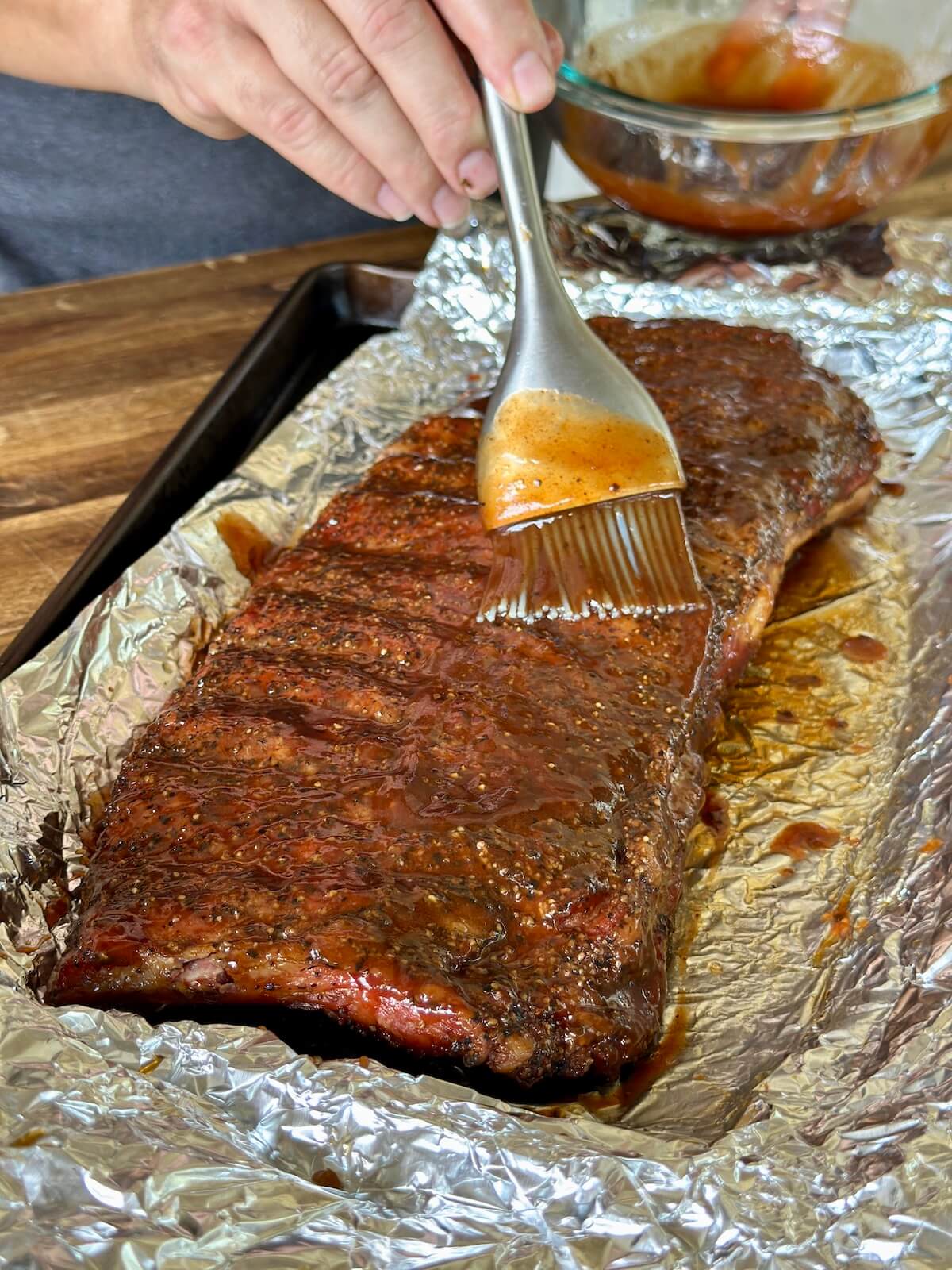 brushing BBQ sauce on to a rack of smoked pork ribs