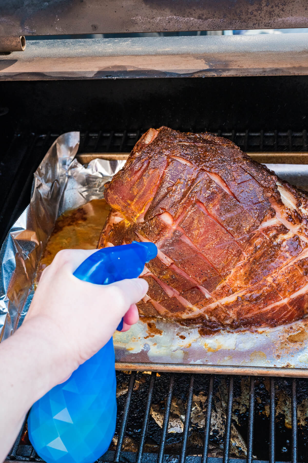 spritzing a smoked ham on a pellet grill