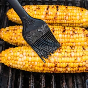 brushing seasoned butter on grilled corn on the cob