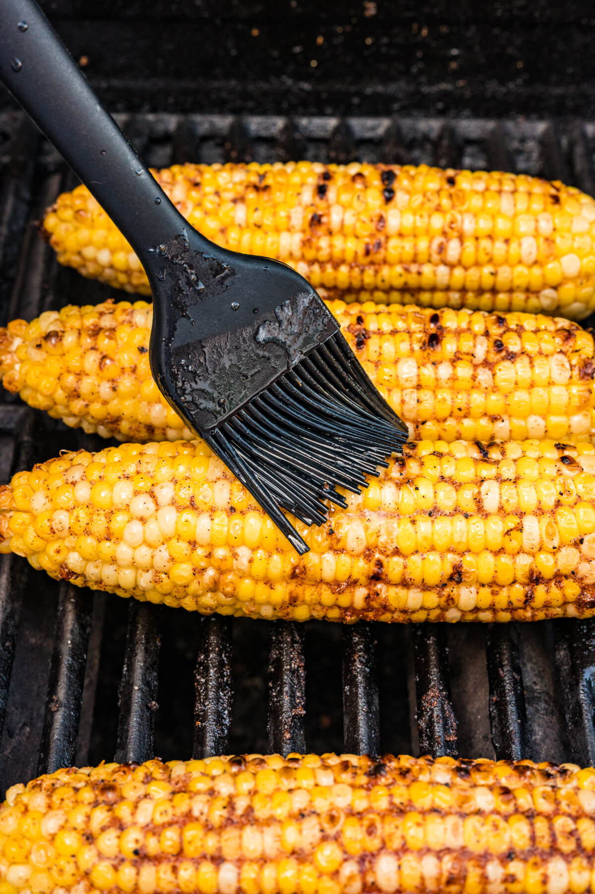 brushing seasoned butter on grilled corn