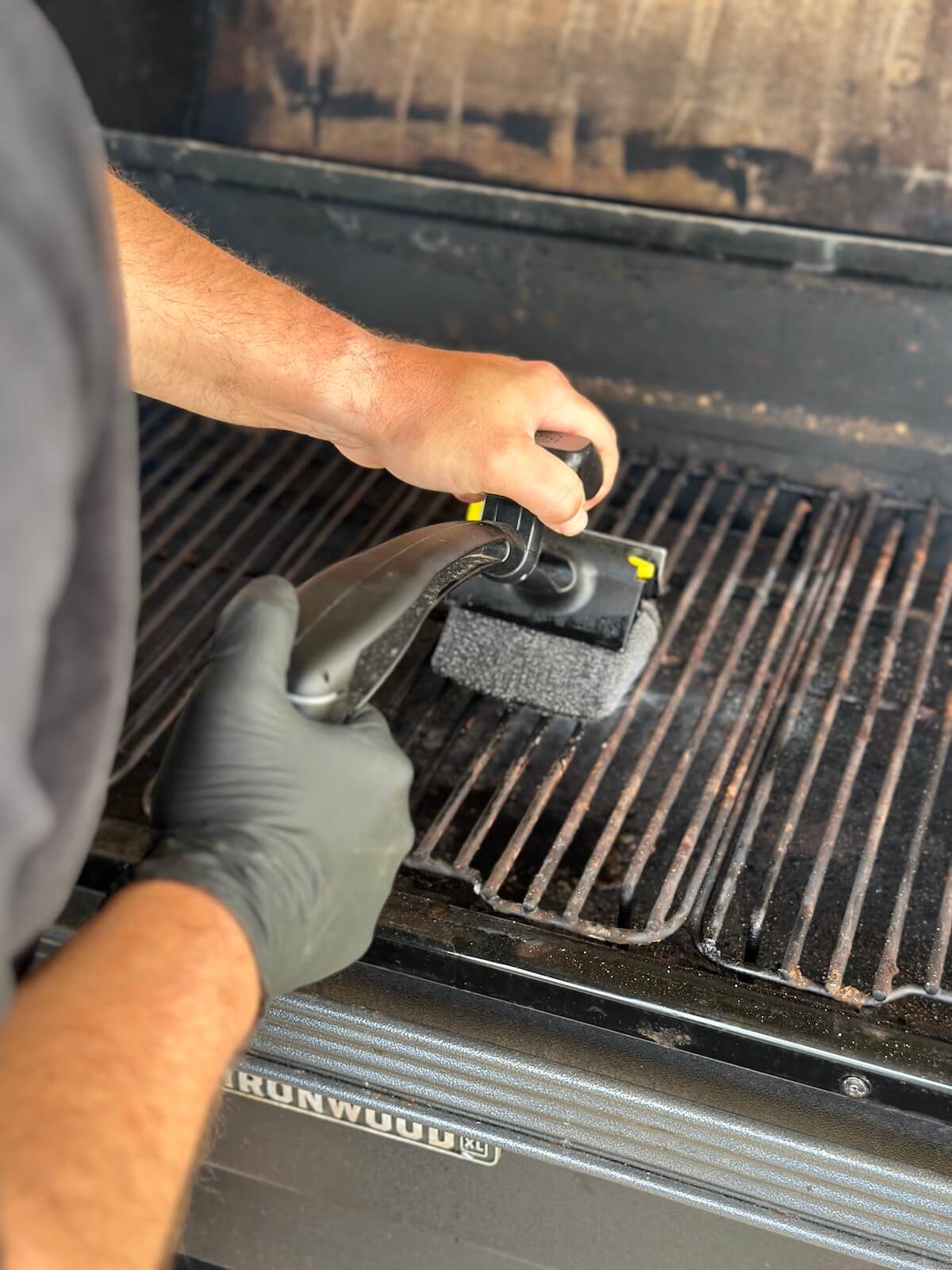 using a grill brush to scrub warm pellet grill grates