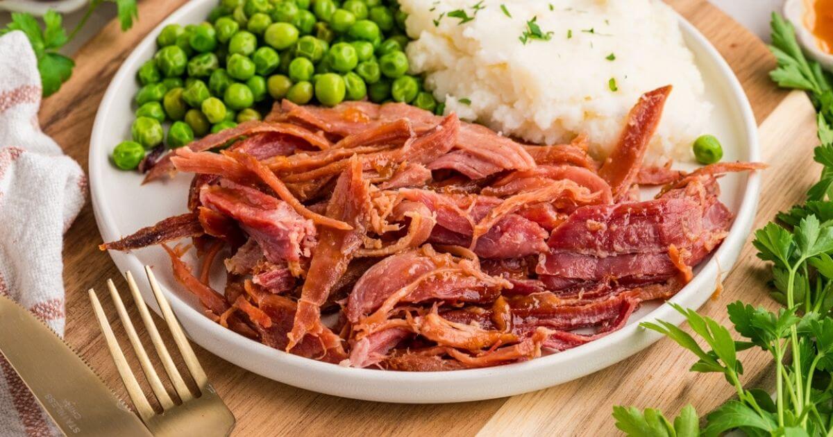 pulled ham on a plate with mashed potatoes and peas