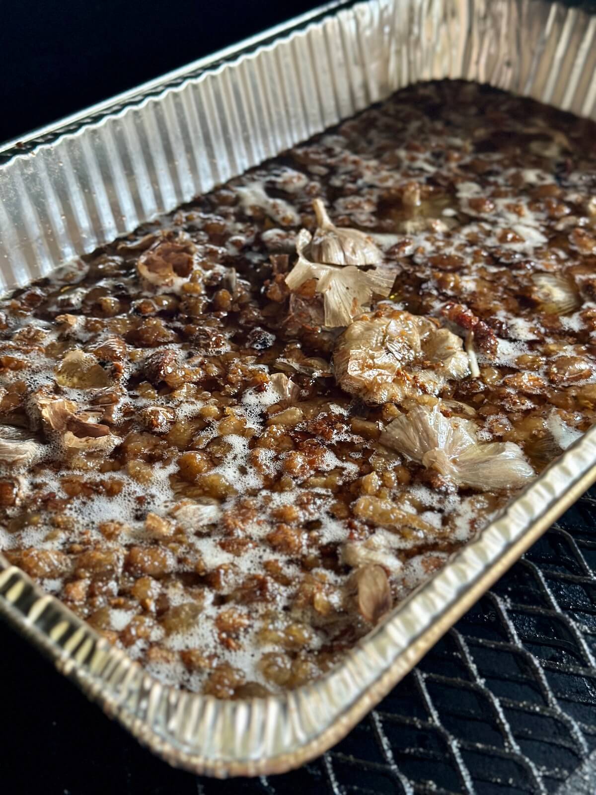 smoked beef tallow in a foil pan with halved heads of garlic