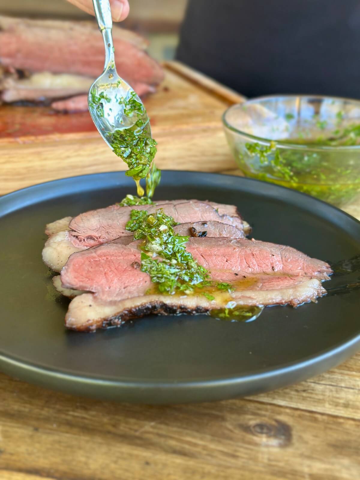 spooning chimichurri sauce onto sliced steak