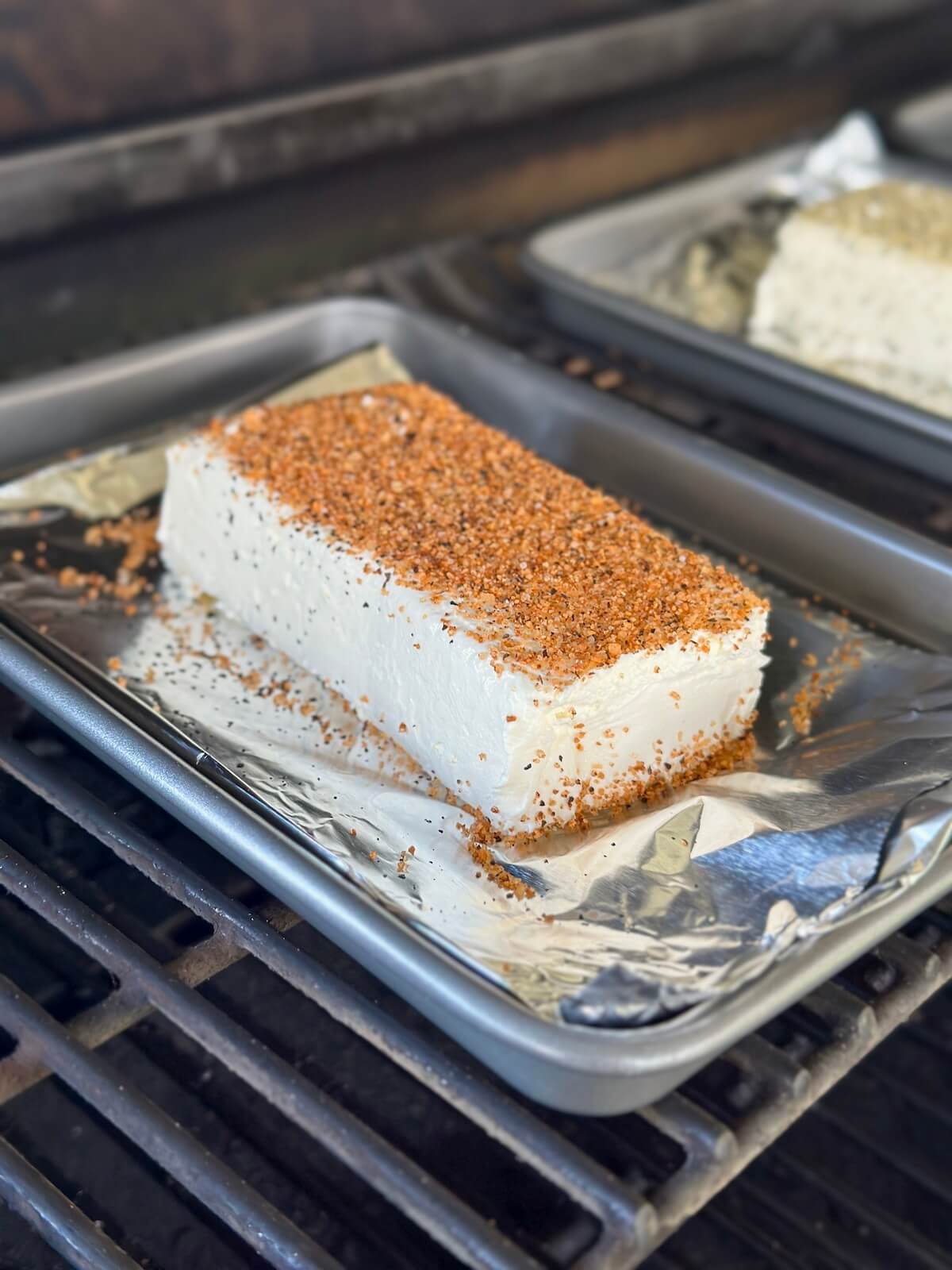 block of cream cheese with barbecue seasoning on top of a foil-lined small sheet tray