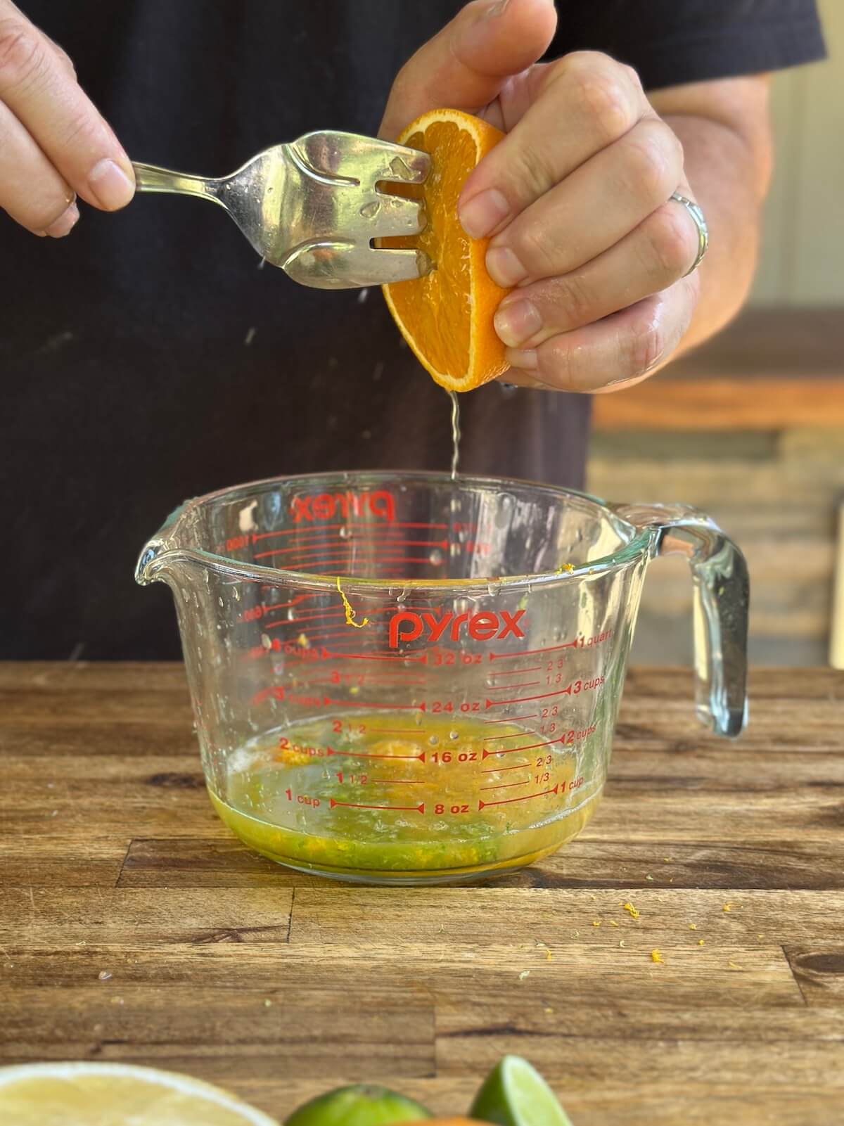 squeezing orange juice into a glass measuring cup with lime juice