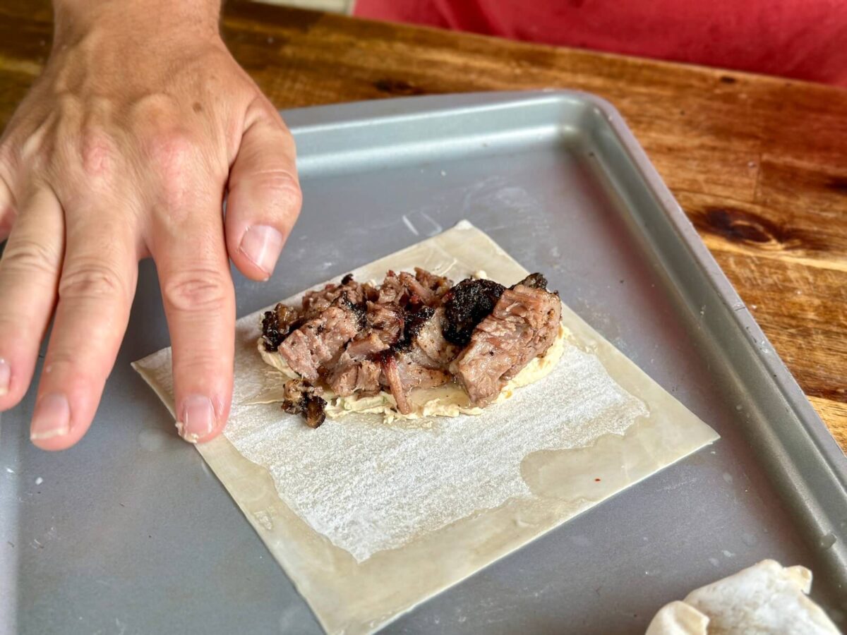 adding water to the outer edge of an egg roll wrapper with cream cheese and brisket on the inside