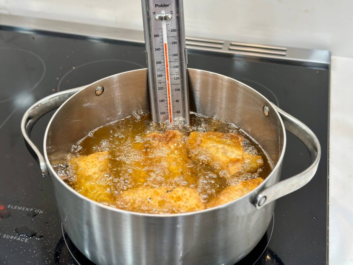 frying egg rolls in a large pot with a frying thermometer