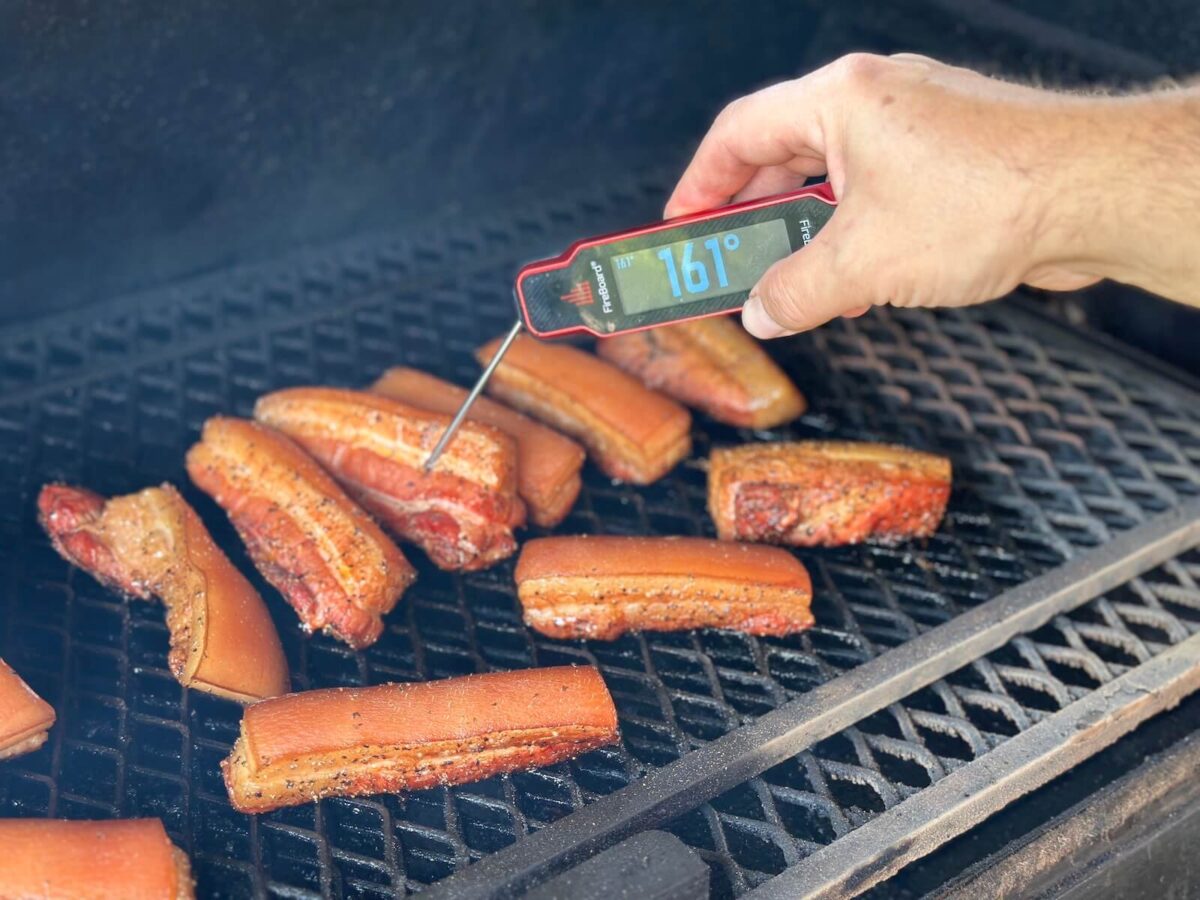 checking the internal temperature of smoked pork belly with an instant read thermometer