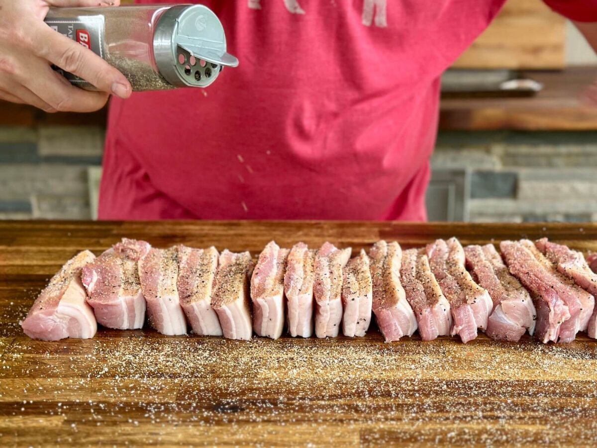 seasoning strips of pork belly on a cutting board