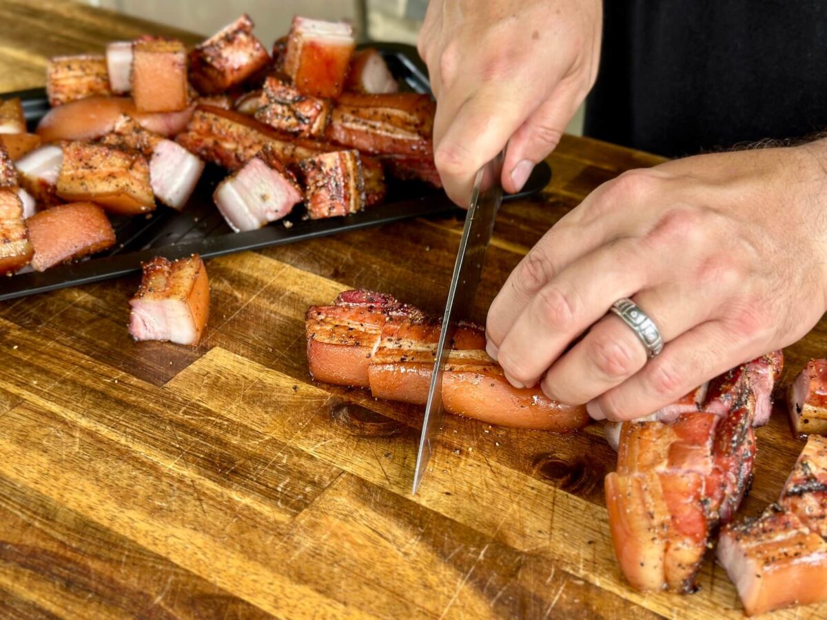 cutting strips of smoked pork belly into cubes