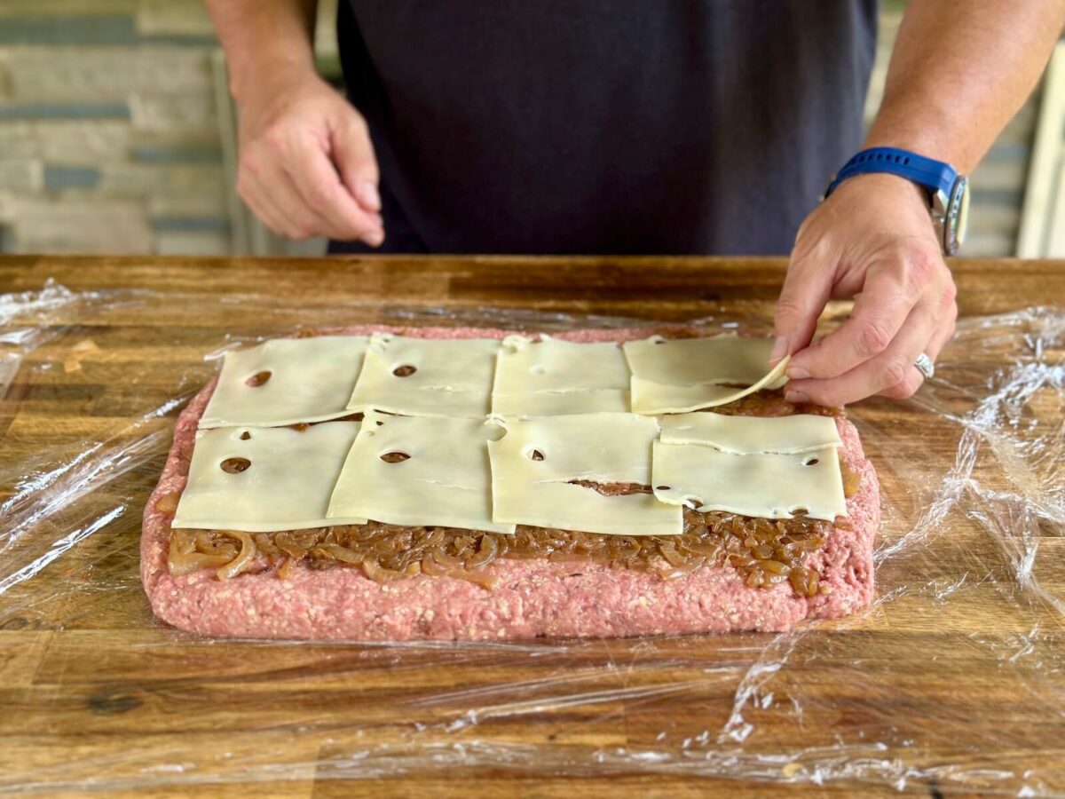 laying Swiss cheese slices on top of ground beef in a thin layer