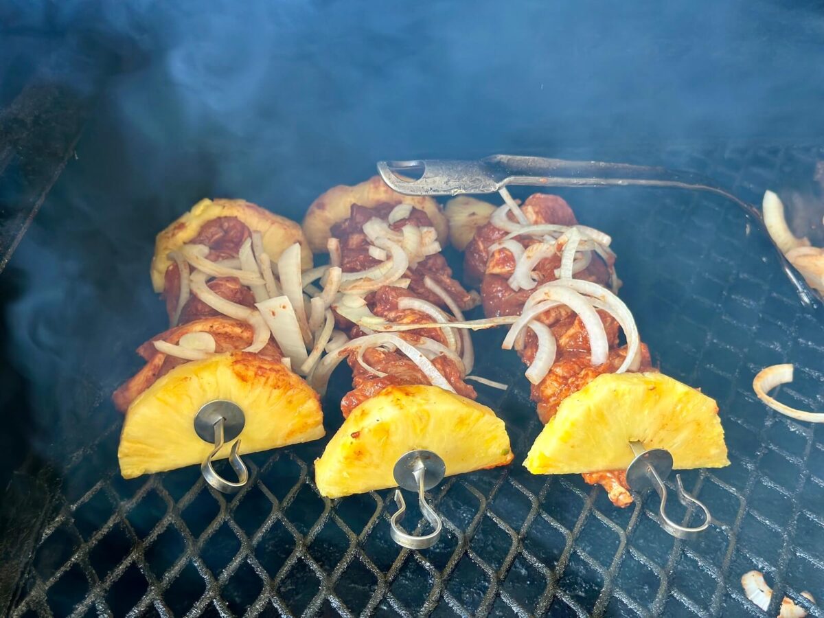 grilling pork al pastor on metal skewers with pineapple slices