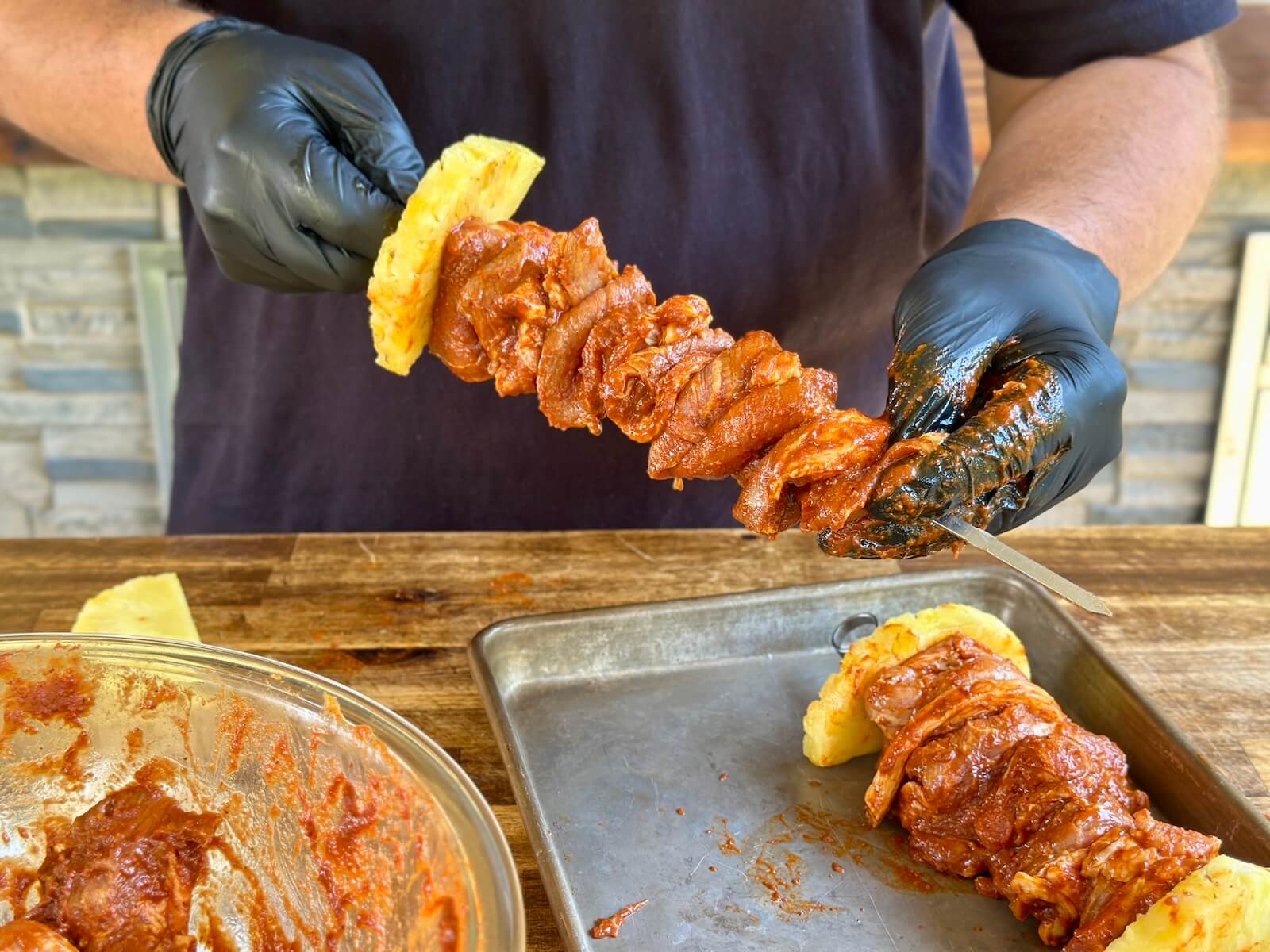 skewering thinly sliced pieces of pork shoulder with al pastor marinade