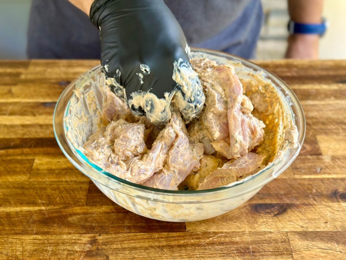 mixing chicken in a large bowl with Greek yogurt marinade