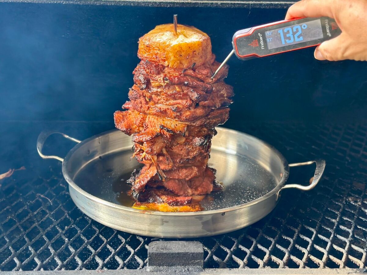 using an instant read meat thermometer to check the internal temp of al pastor on a skewer