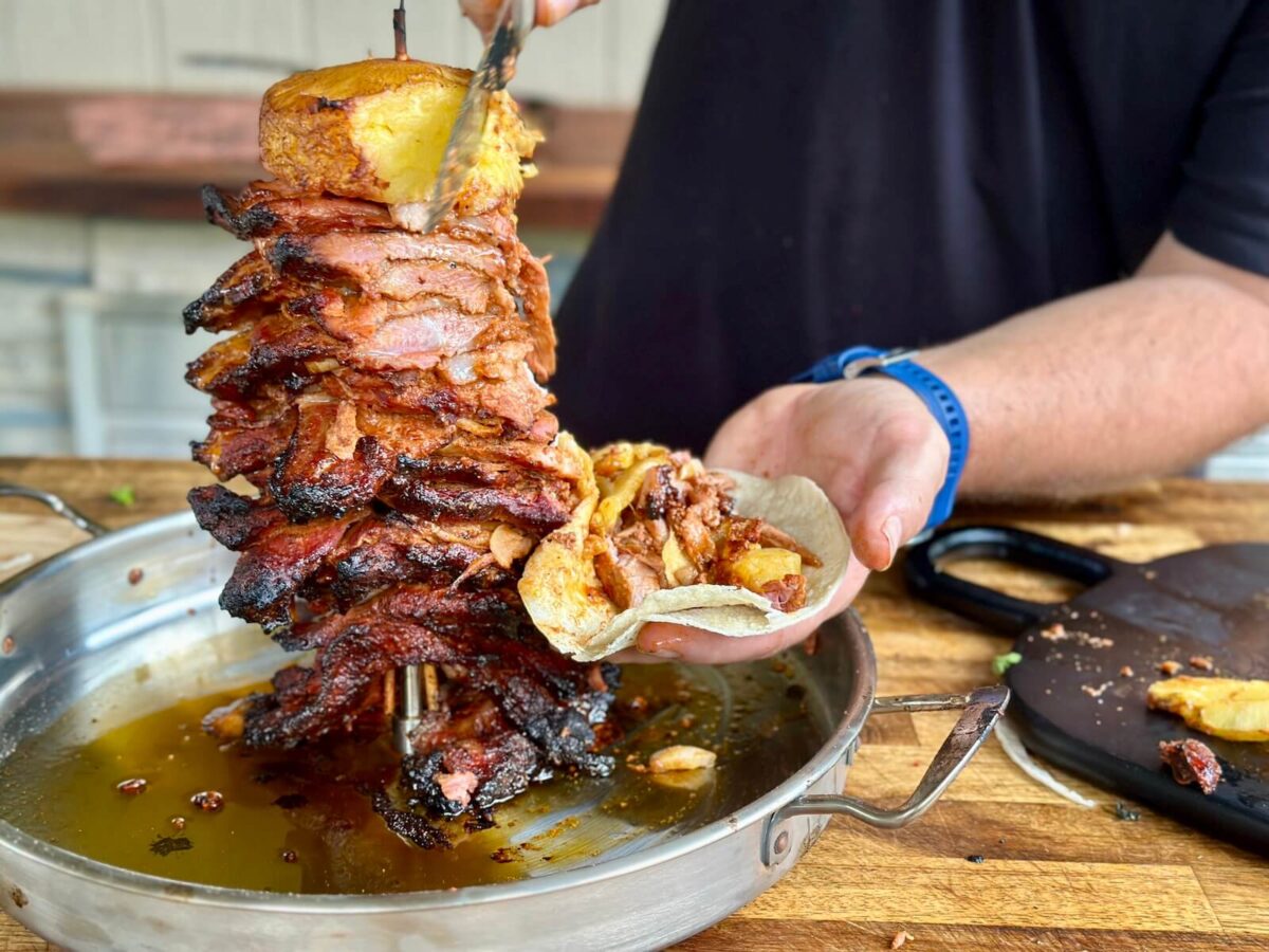 slicing grilled al pastor on a vertical skewer for tacos