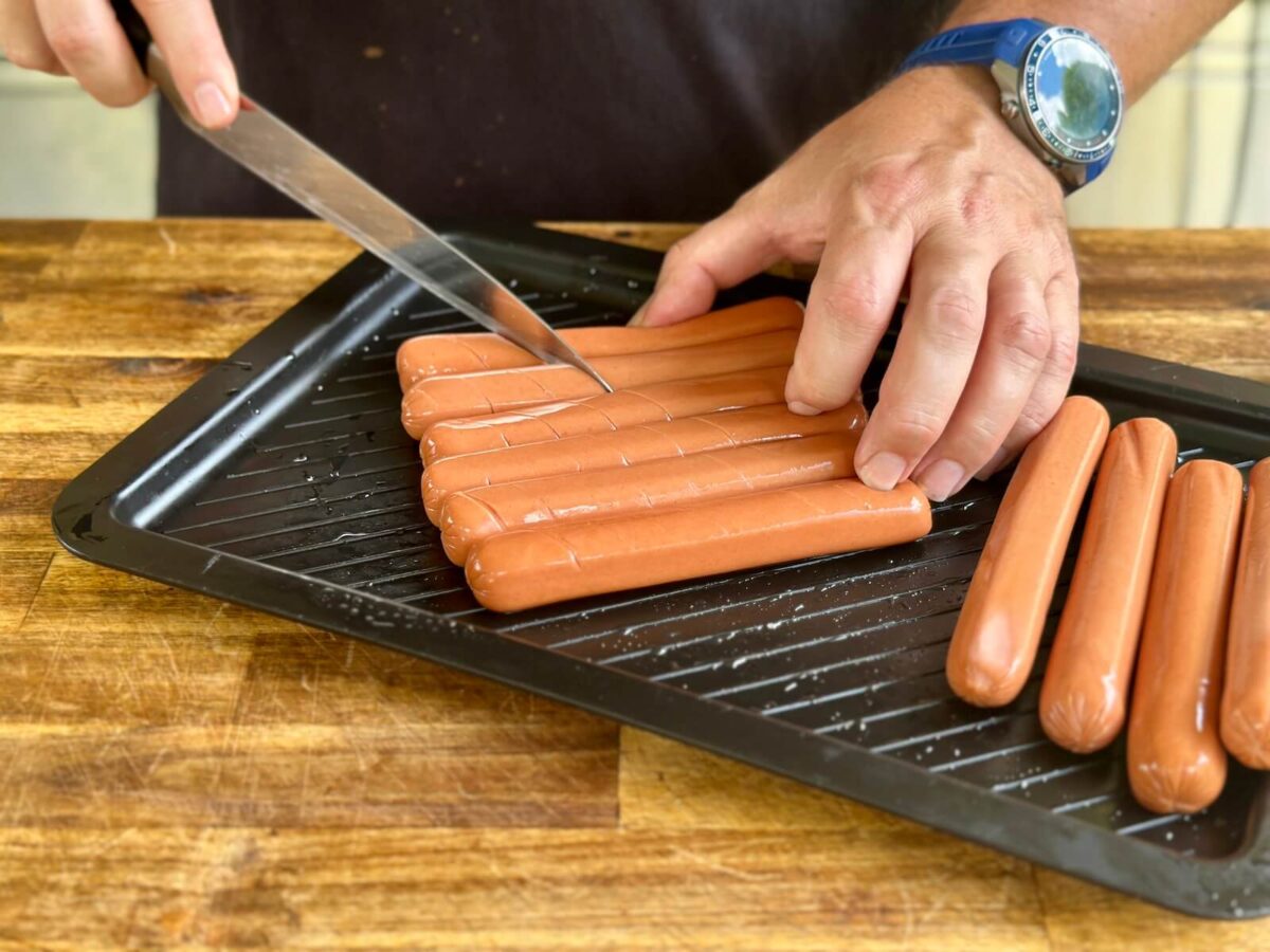 using a knife to make diagonal slits in the surface of hot dogs