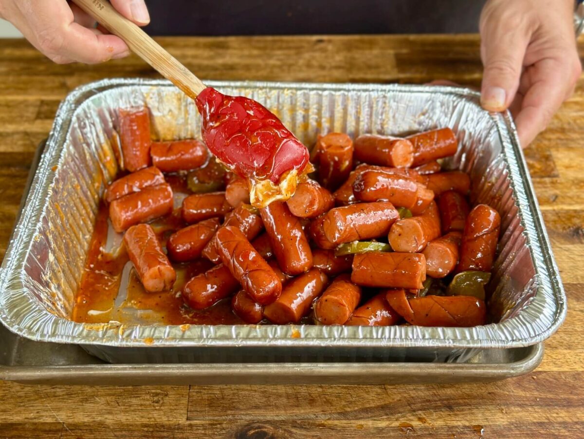 mixing smoked hot dogs with barbecue sauce, brown sugar, and butter in a foil pan