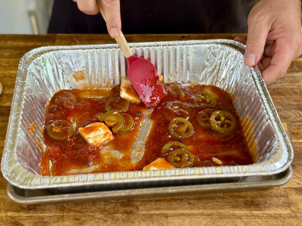 mixing barbecue sauce, butter, brown sugar, and jalapeno slices in an aluminum foil pan