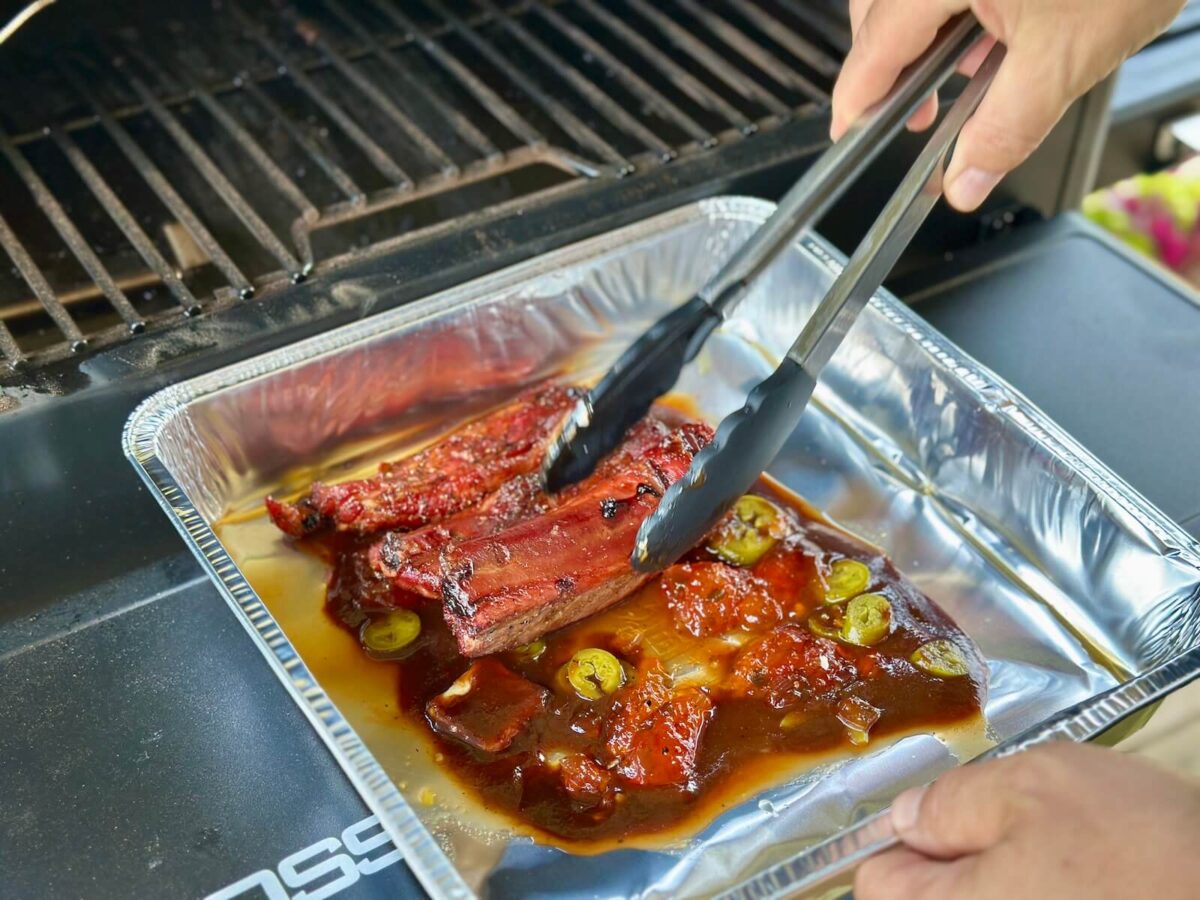 adding smoked party ribs to a foil pan with bbq sauce