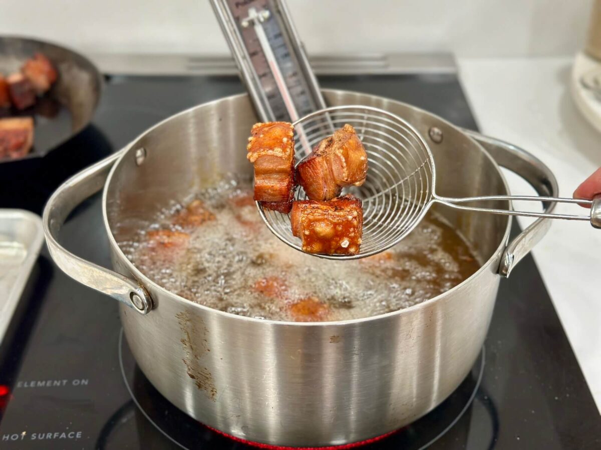 frying small cubes of smoked pork belly in a large pot of oil