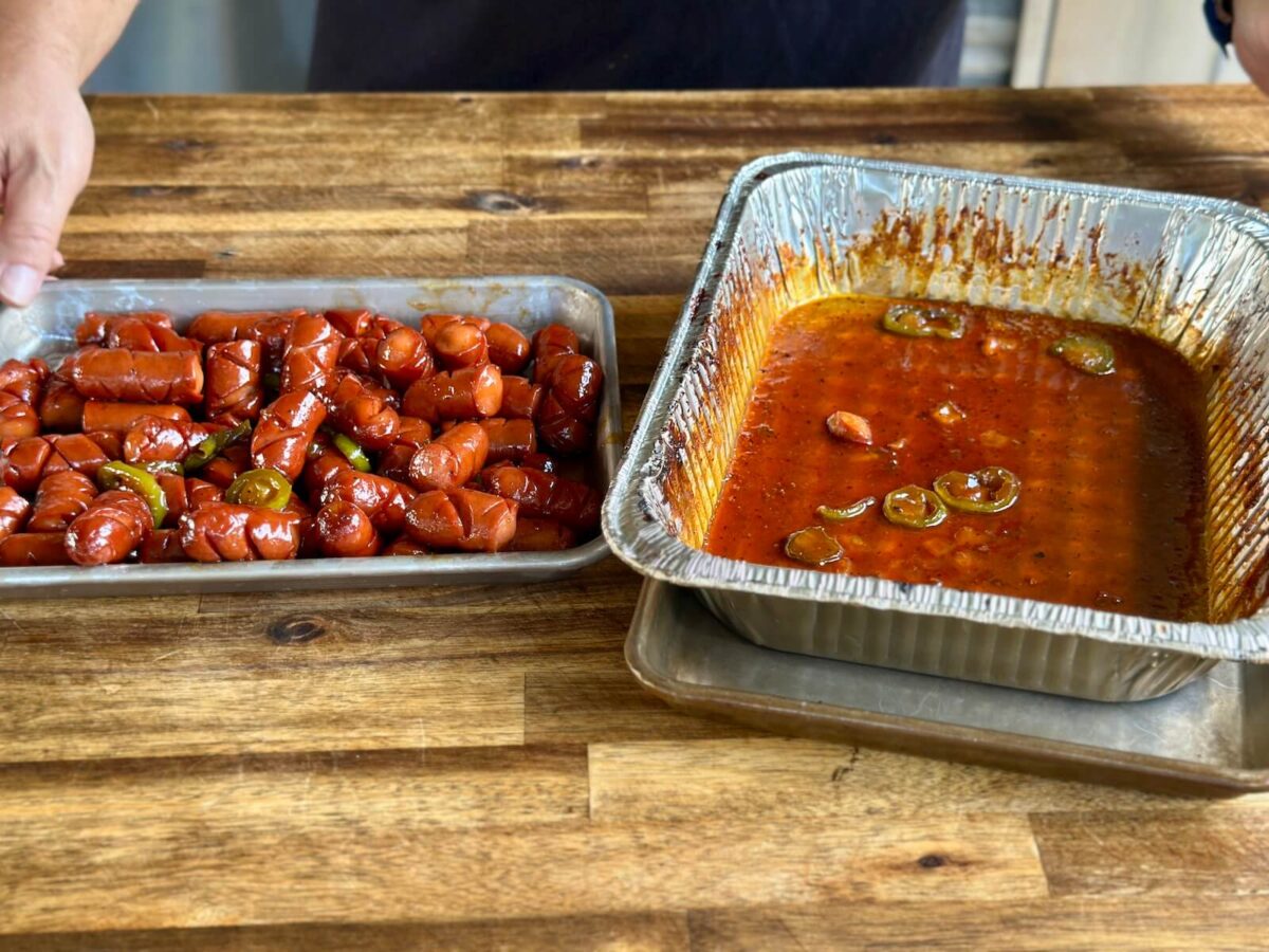 an aluminum foil pan with burnt ends sauce and a small sheet tray with cut up smoked hot dogs