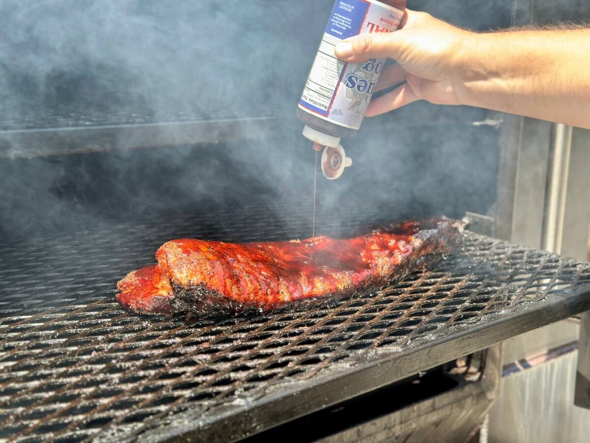 adding barbecue sauce to smoked pork belly on a smoker