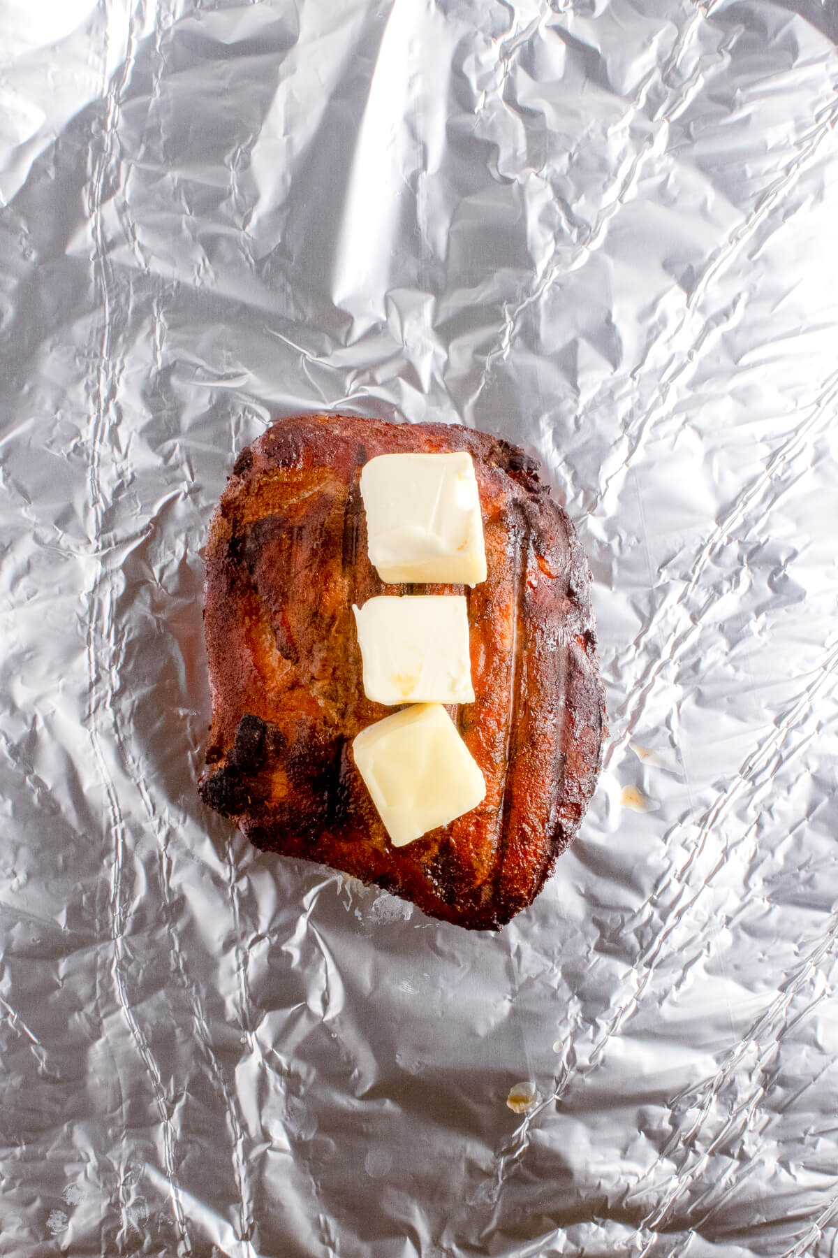 smoked turkey breast with slices of butter on top, getting wrapped in a piece of aluminum foil