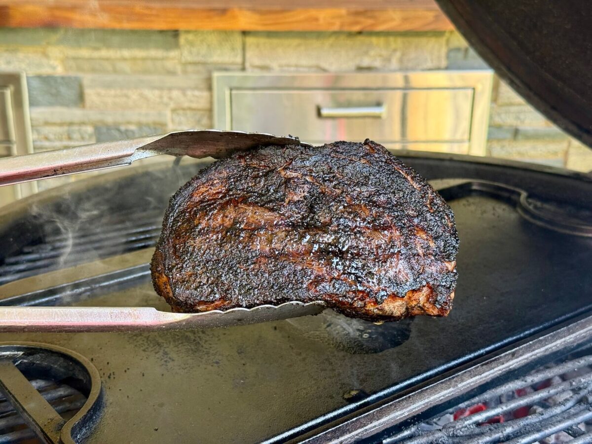ribeye steak with a very dark steak crust cooking on a cast iron griddle on top of a charcoal grill