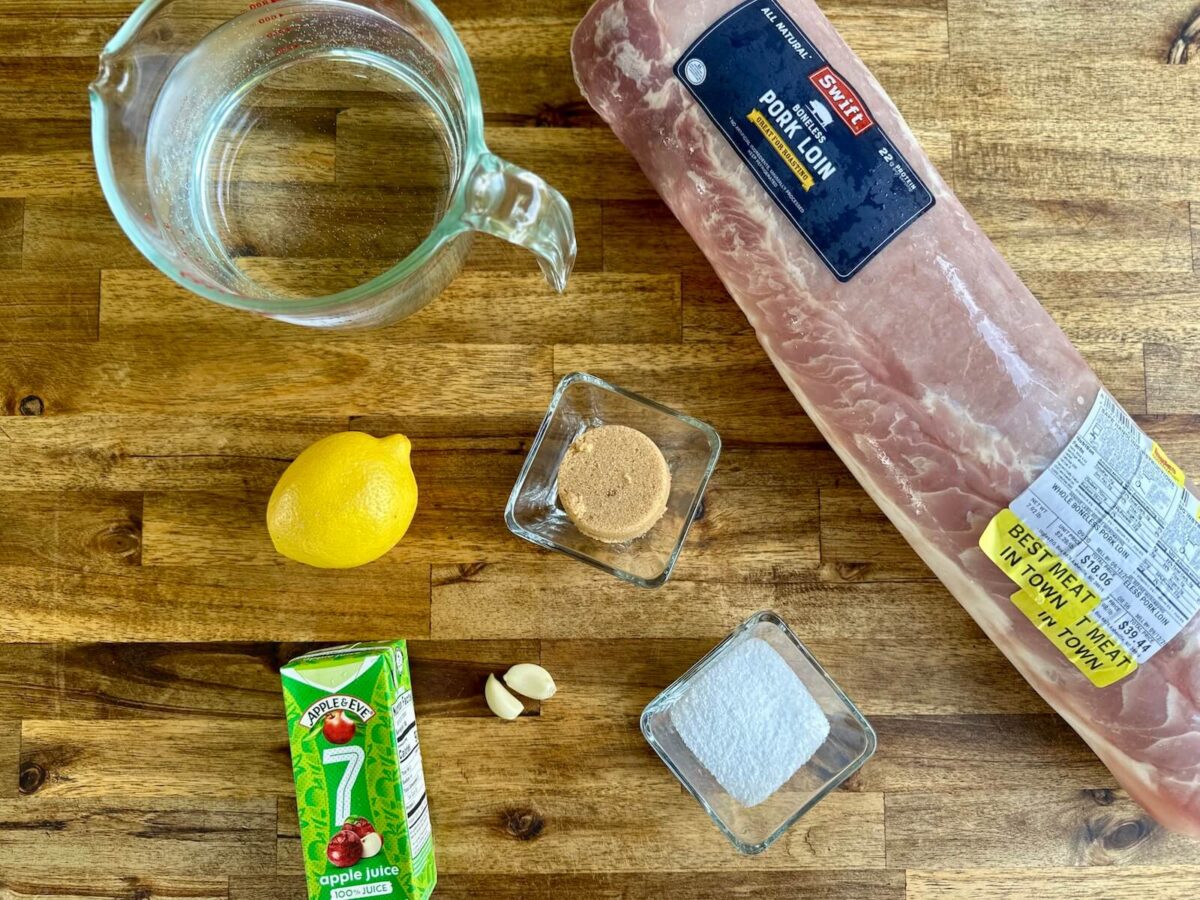 pork loin with ingredients for a brine including water, salt, brown sugar, lemon, garlic, and apple juice