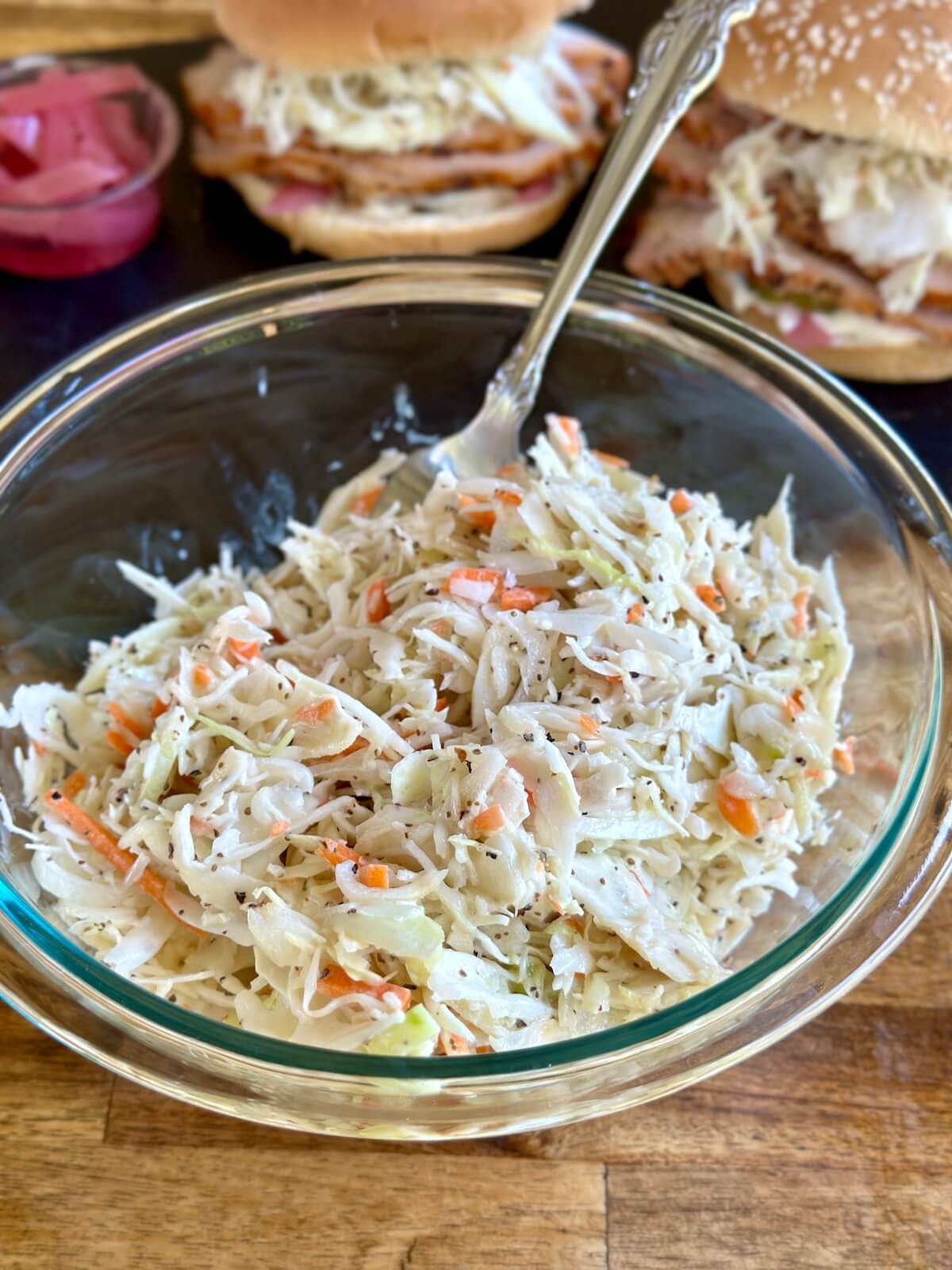coleslaw in a bowl with pulled pork sandwiches in the background