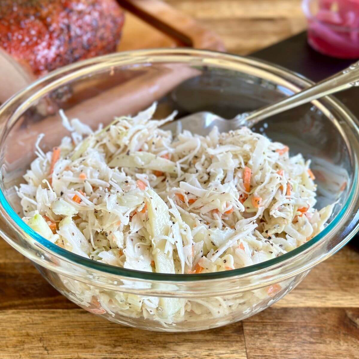 coleslaw in a bowl with pork in the background