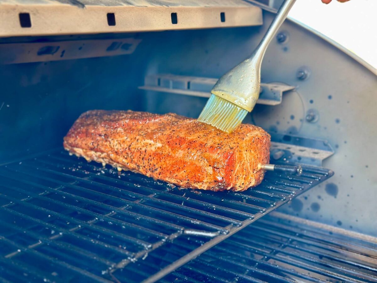 using a pastry brush to glaze a smoked pork loin on a pellet grill
