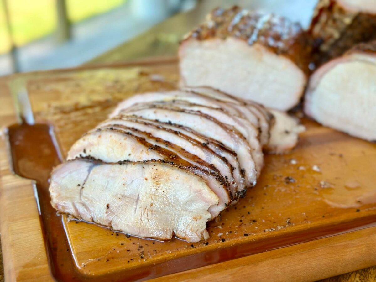 smoked pork loin sliced on a cutting board with juices on the board