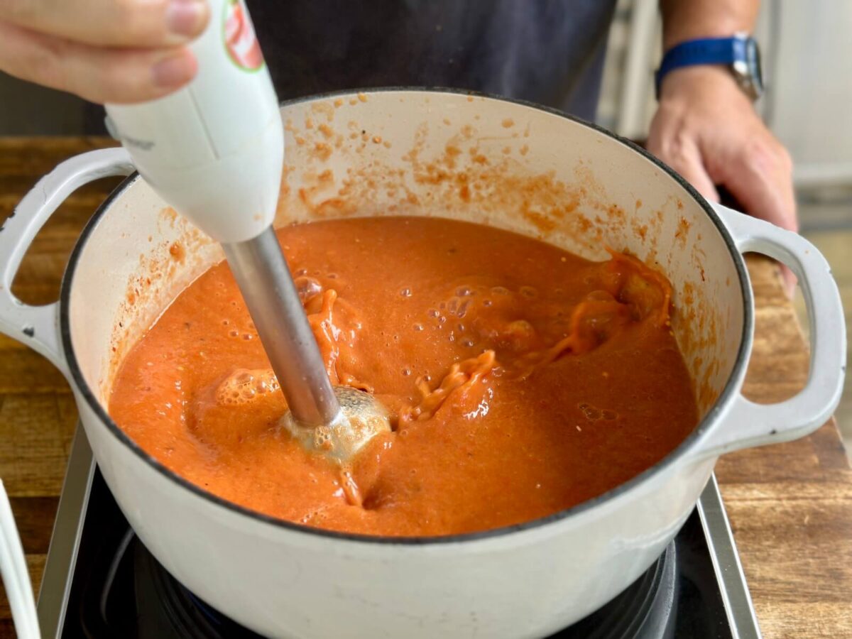 using an immersion blender to blend smoked tomatoes in a Dutch oven