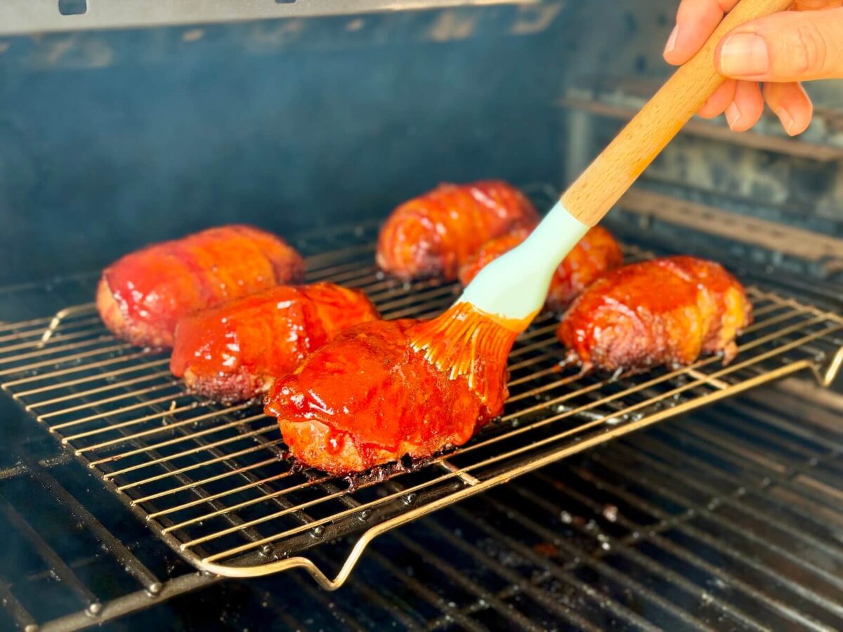 brushing a bbq glaze on armadillo eggs on a pellet grill